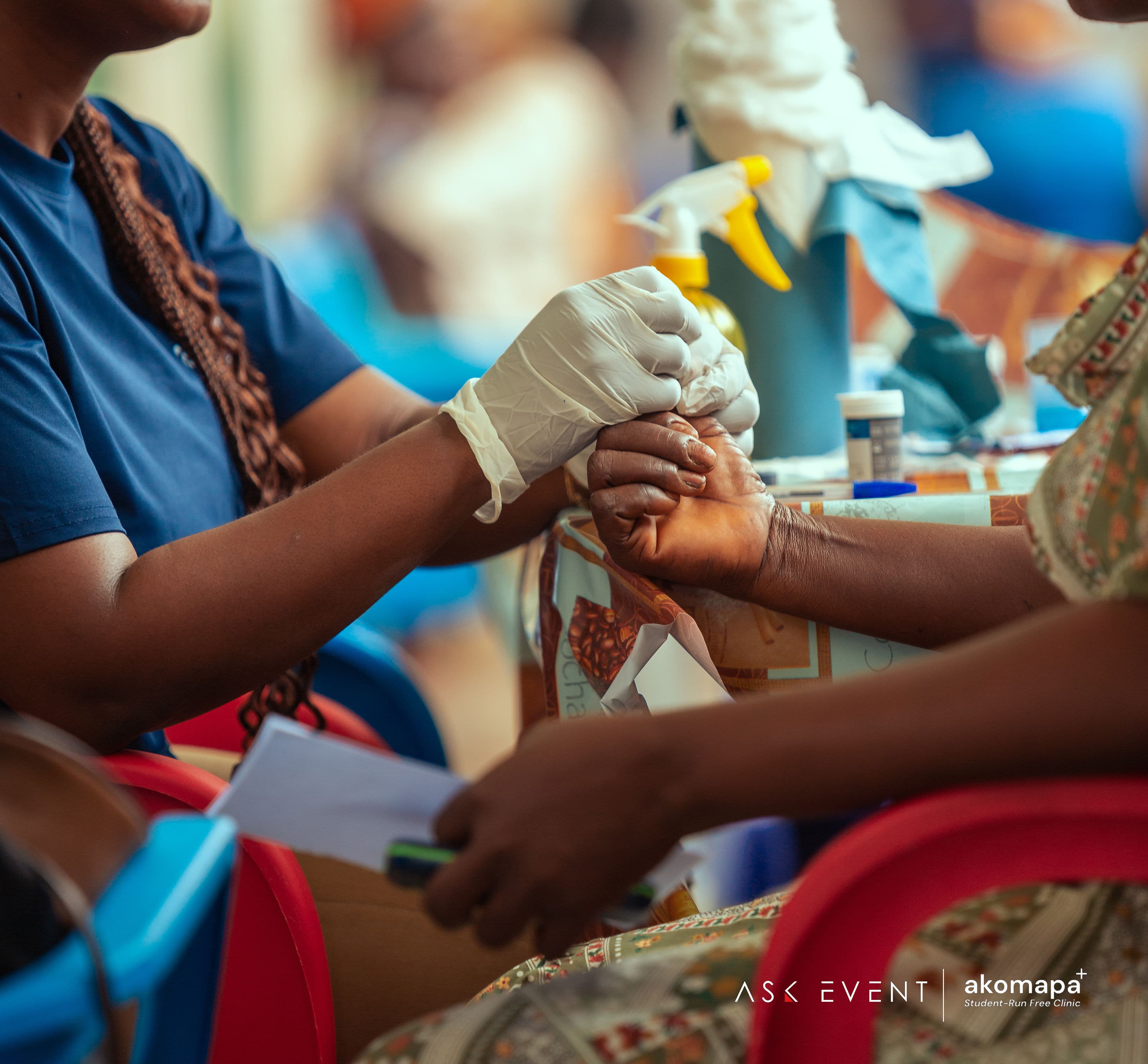 Healthcare worker examining a patient's hand during a glucose screening at an Akomapa community clinic